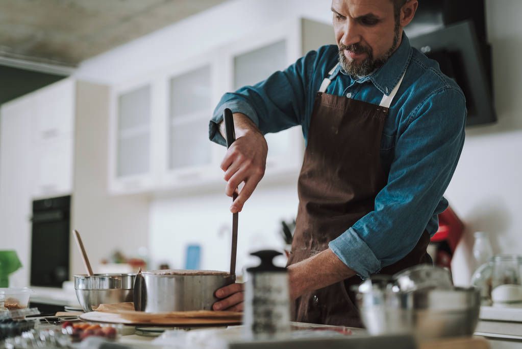 Koncentrovaný muž s použitím rozmetatele šlehačku během vaření - Fotografie, Obrázek