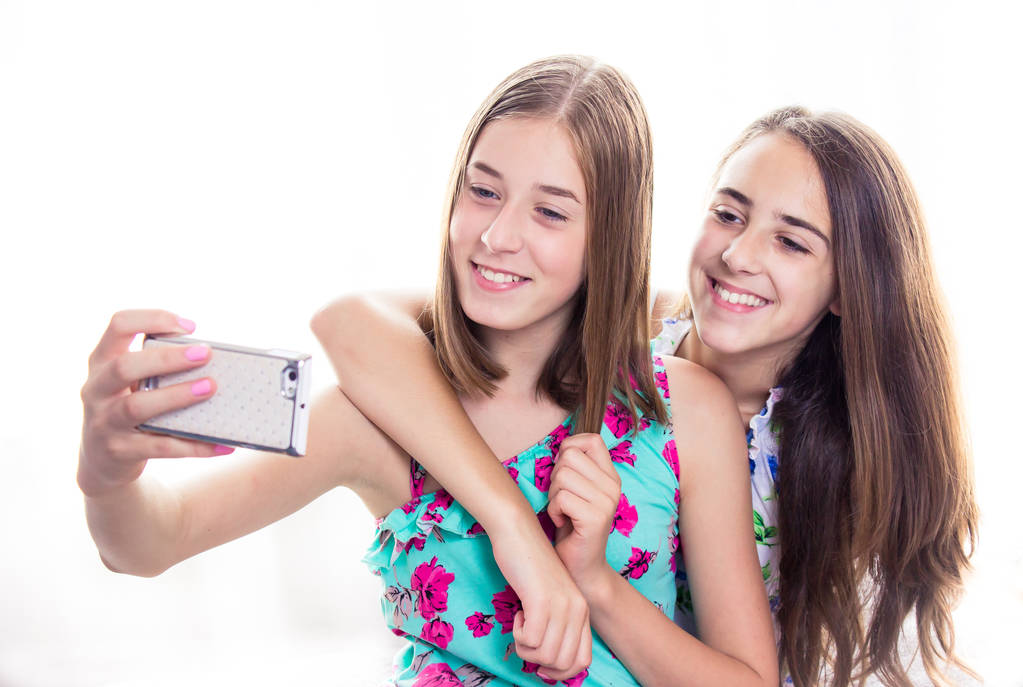 İki kız akıllı telefona bakıyor, selfie çekiyor. Sosyal medya kavramı - Fotoğraf, Görsel