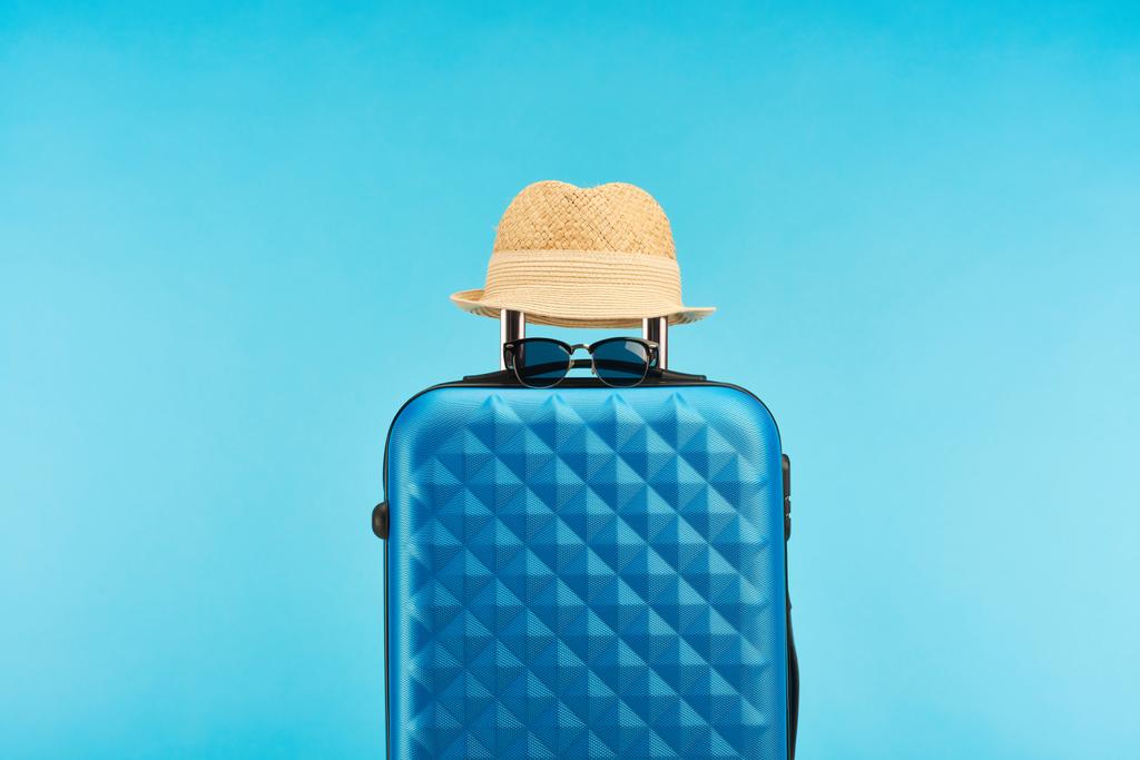 blue colorful travel bag with handle, sunglasses and straw hat isolated on blue  - Photo, Image
