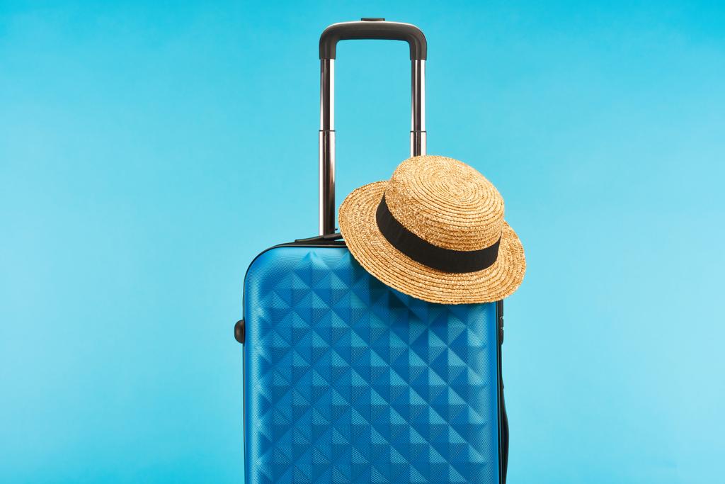 μπλε πολύχρωμη τσάντα ταξιδιού με λαβή και ψάθινο καπέλο απομονωθεί σε μπλε  - Φωτογραφία, εικόνα
