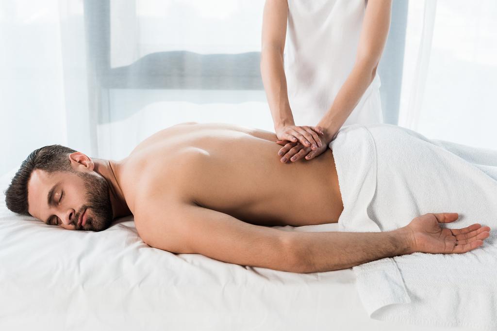 обрезанный вид массажера, делающего массаж бородатому мужчине лежащему на массажном столе
  - Фото, изображение