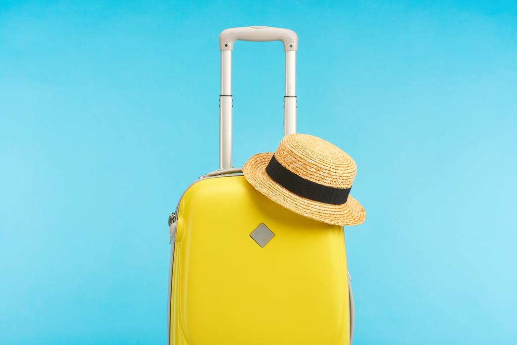 yellow travel bag with straw hat isolated on blue - Photo, Image