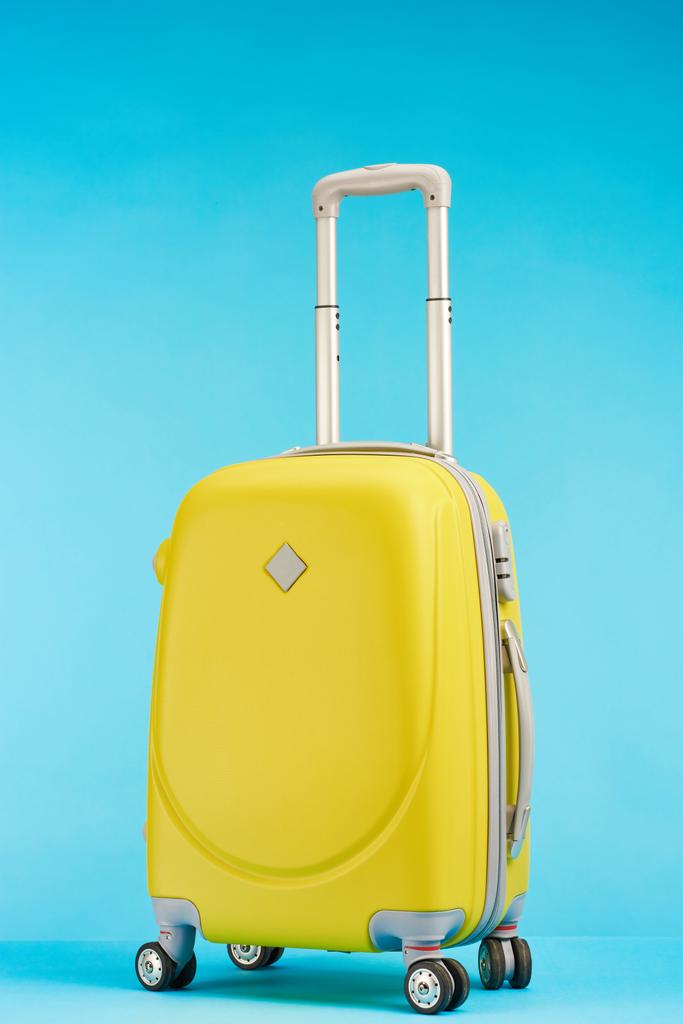 yellow colorful travel bag with handle on wheels on blue background - Photo, Image