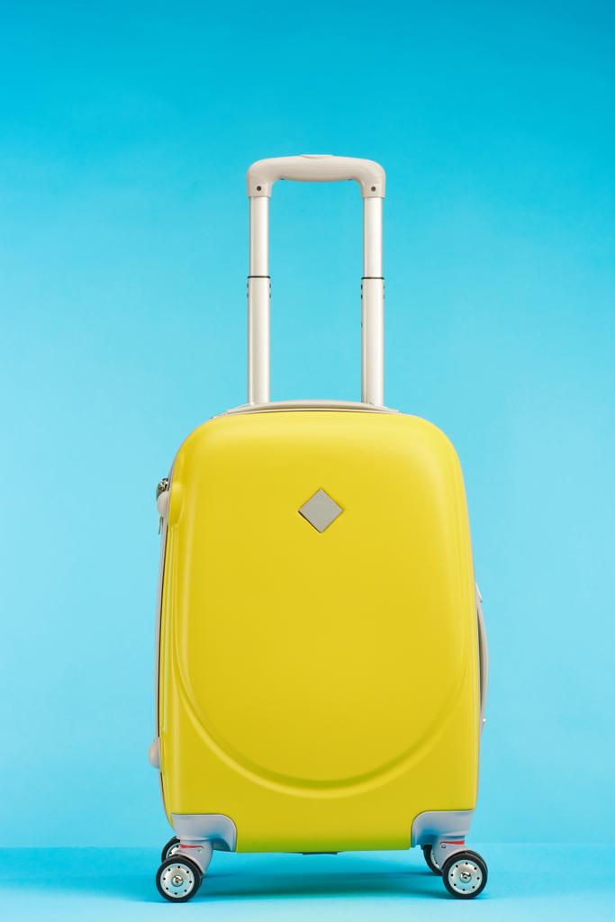 żółta walizka z uchwytem na kółkach na niebieskim tle - Zdjęcie, obraz