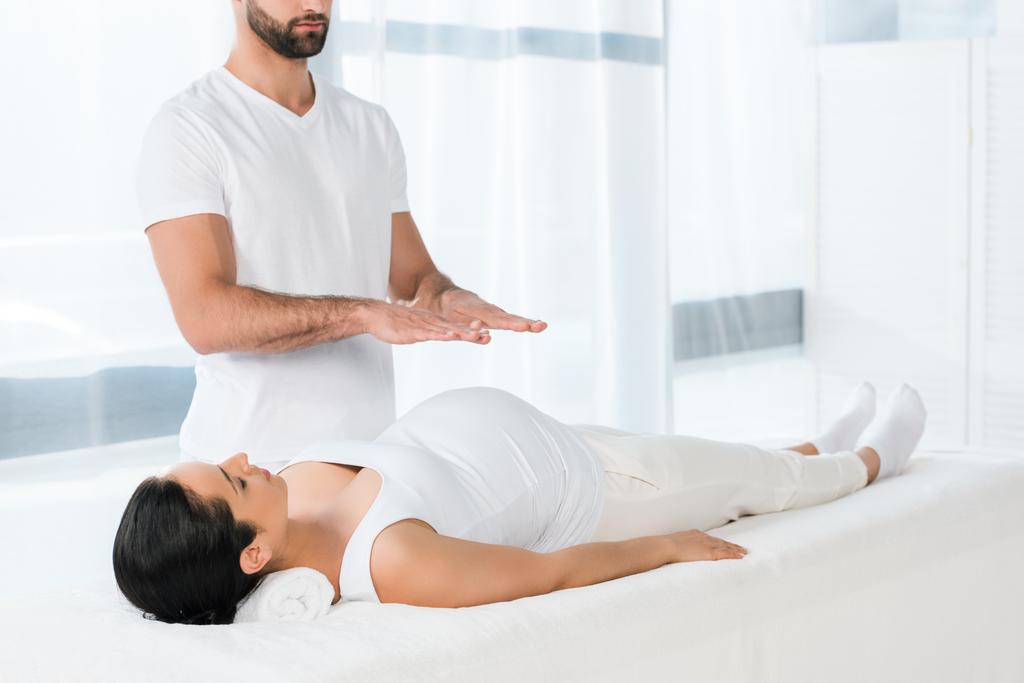 bebaarde man Healing brunette zwangere vrouw liggend op massagetafel  - Foto, afbeelding