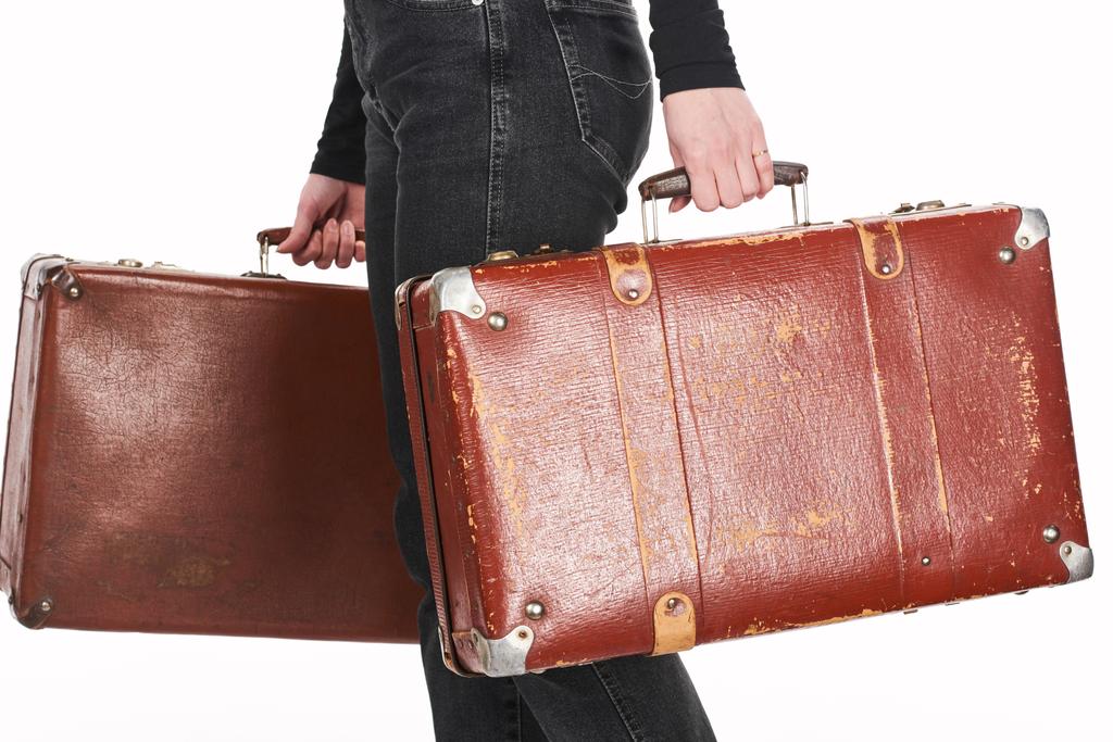 cropped view of woman in jeans holding vintage weathered suitcases isolated on white - Photo, Image