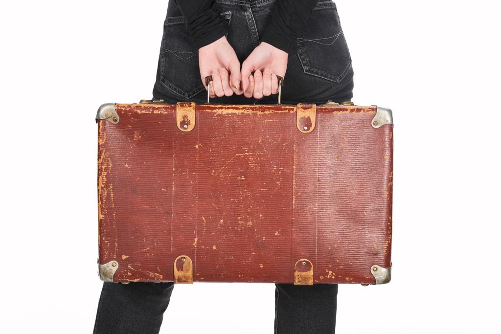 partial view of woman in jeans holding vintage leather suitcase isolated on white - Photo, Image