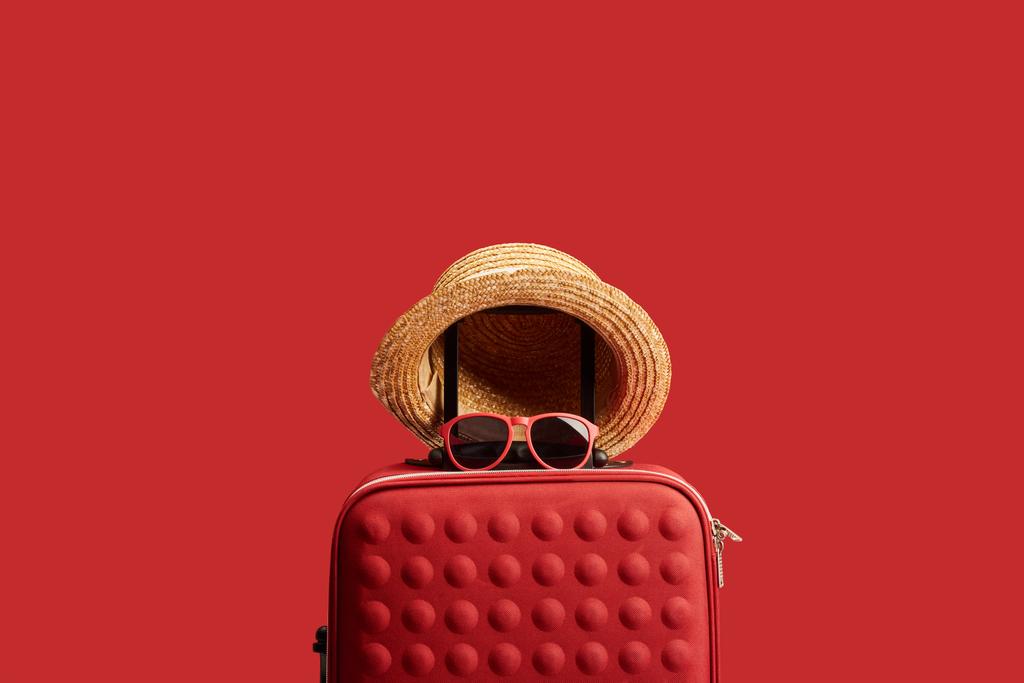麦わら帽子とサングラスが赤で隔離された赤いカラフルな旅行バッグ  - 写真・画像
