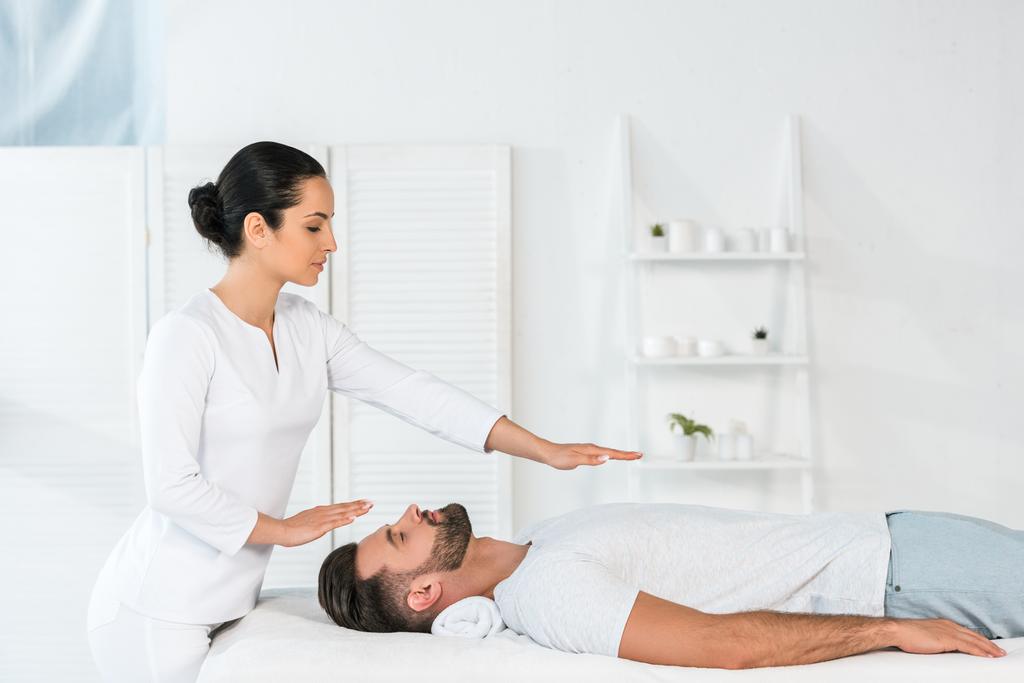 attractive healer putting hands above body of handsome man on massage table - Photo, Image