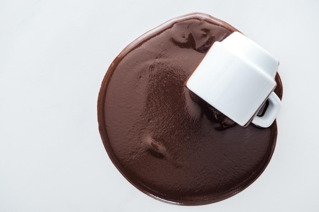 Вид сверху чашки с разливающимся шоколадом на белом фоне
  - Фото, изображение