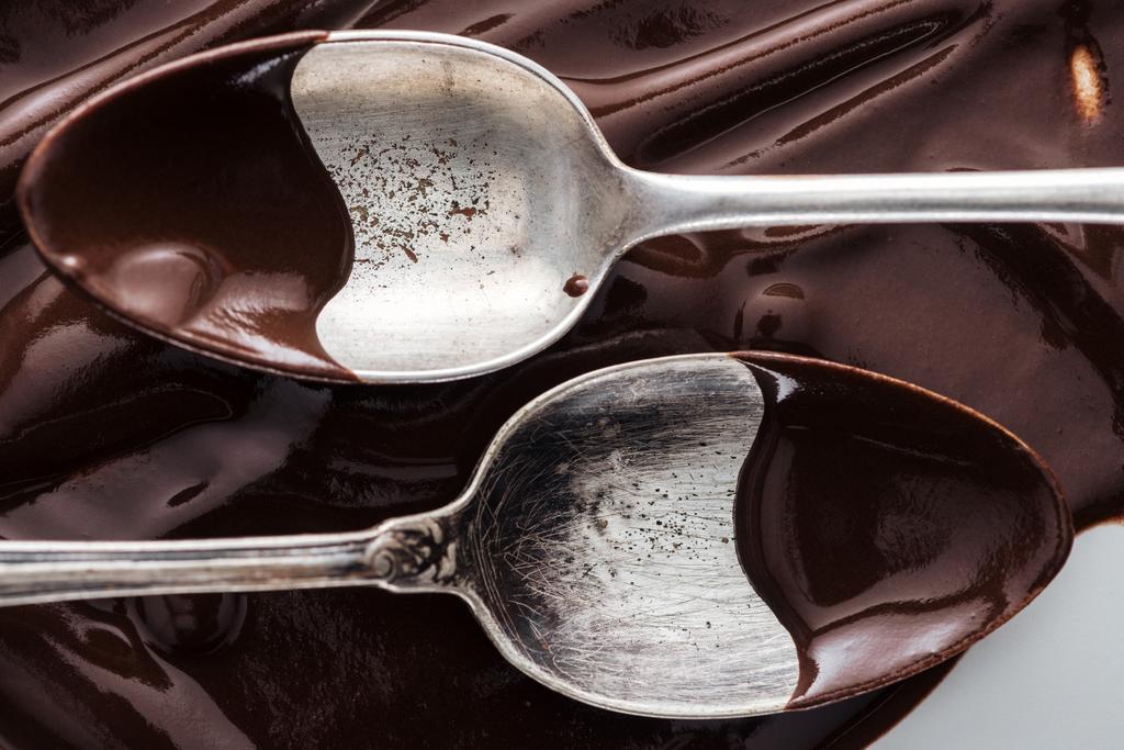 Vista de cerca de cucharas cubiertas de chocolate sobre fondo de chocolate derretido
 - Foto, imagen