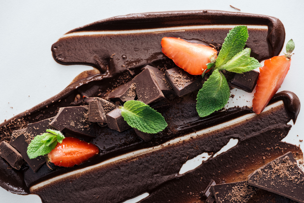 チョコレートバー、イチゴ、グリーンミントのピースと溶けたチョコレートのトップビュー - 写真・画像