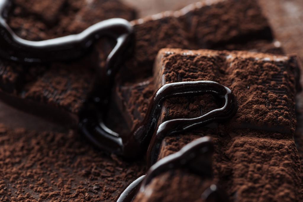 Close up view of pieces of dark chocolate bar with melted chocolate and cocoa powder - Photo, Image