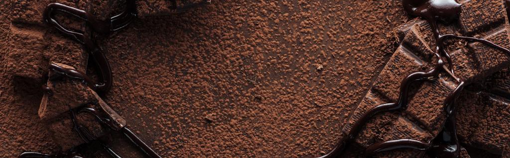 Tiro panorâmico de pedaços de barra de chocolate com chocolate derretido e cacau em pó
 - Foto, Imagem