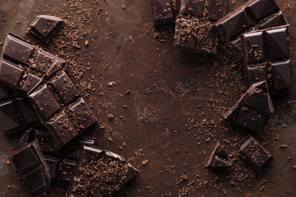 Vista superior de trozos de barra de chocolate con virutas de chocolate sobre fondo de metal oxidado
  - Foto, imagen