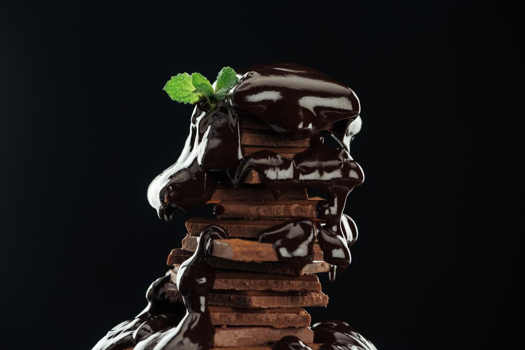 dunkler Schokoladenstapel mit geschmolzener Schokolade und frischer Minze isoliert auf schwarz - Foto, Bild