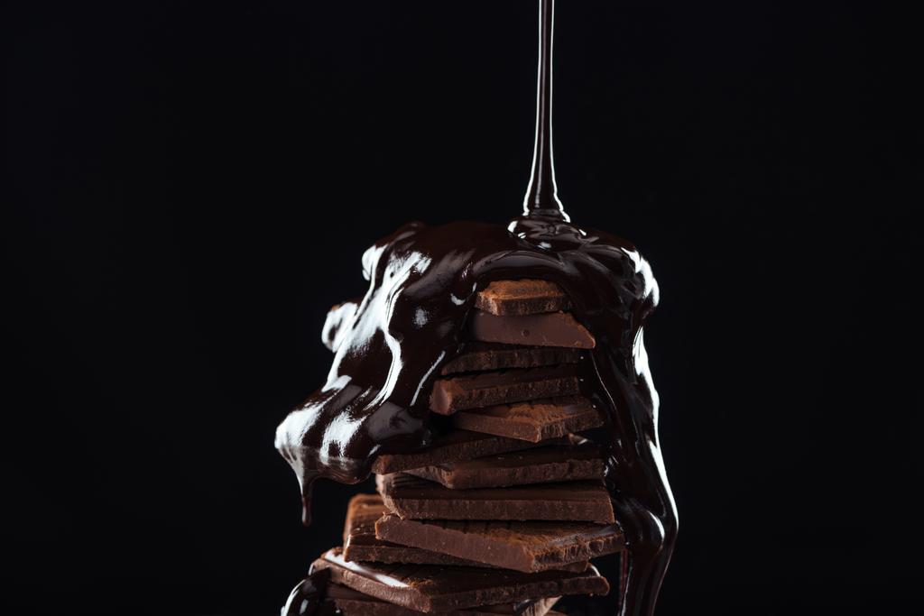 Hot melted chocolate pouring on chocolate stack, isolated on black - Photo, Image