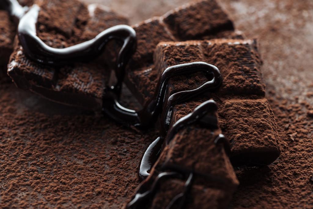 Selectieve focus van stukjes chocoladereep met gesmolten chocolade en cacaopoeder op metalen achtergrond - Foto, afbeelding