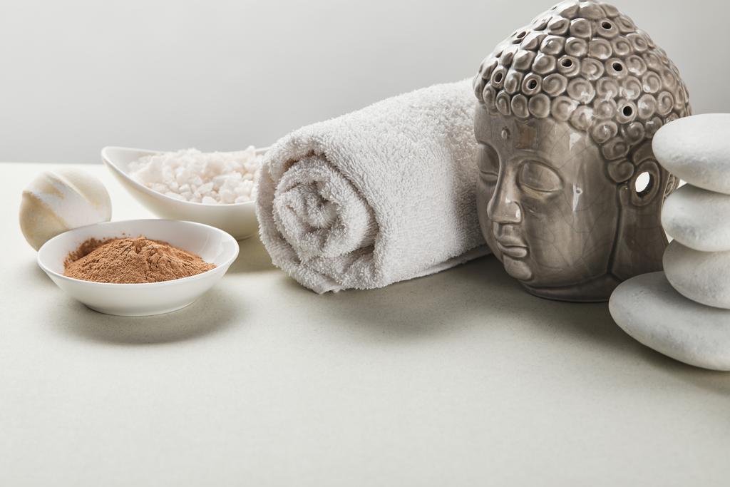 Meersalz und Tonpuder in Schalen, Baumwolltuch, Steinen, Badebombe und Buddha-Figur auf weißem Tisch isoliert auf grau - Foto, Bild