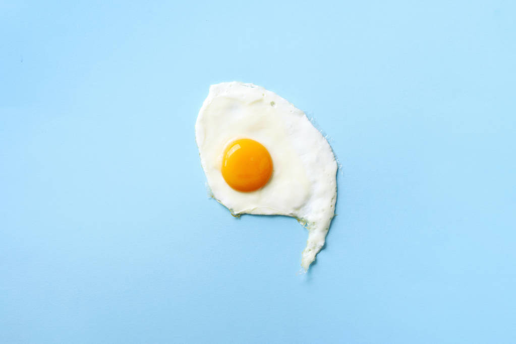 Een gebakken ei op blauwe papieren achtergrond. Creatief voedselconcept in minimale stijl. Bovenaanzicht - Foto, afbeelding