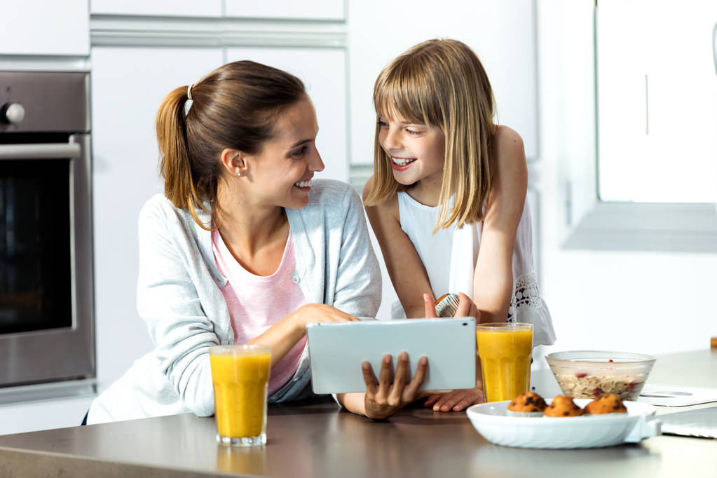 Bella giovane madre e sua figlia utilizzando tablet digitale mentre fanno colazione a casa
.  - Foto, immagini