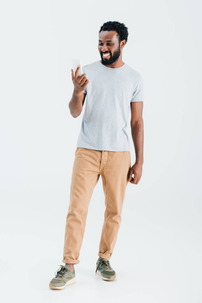 vrolijke Afro-Amerikaanse man met smartphone, geïsoleerd op grijs - Foto, afbeelding