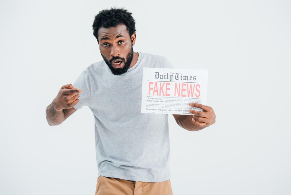 灰色に隔離された偽のニュースで新聞を指差すショックを受けたアフリカ系アメリカ人の男 - 写真・画像