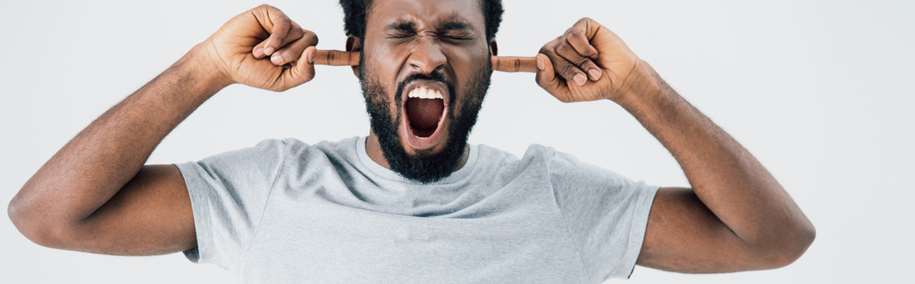 emotivo uomo afroamericano in t-shirt grigia urlando e chiudendo orecchie isolate su grigio
 - Foto, immagini
