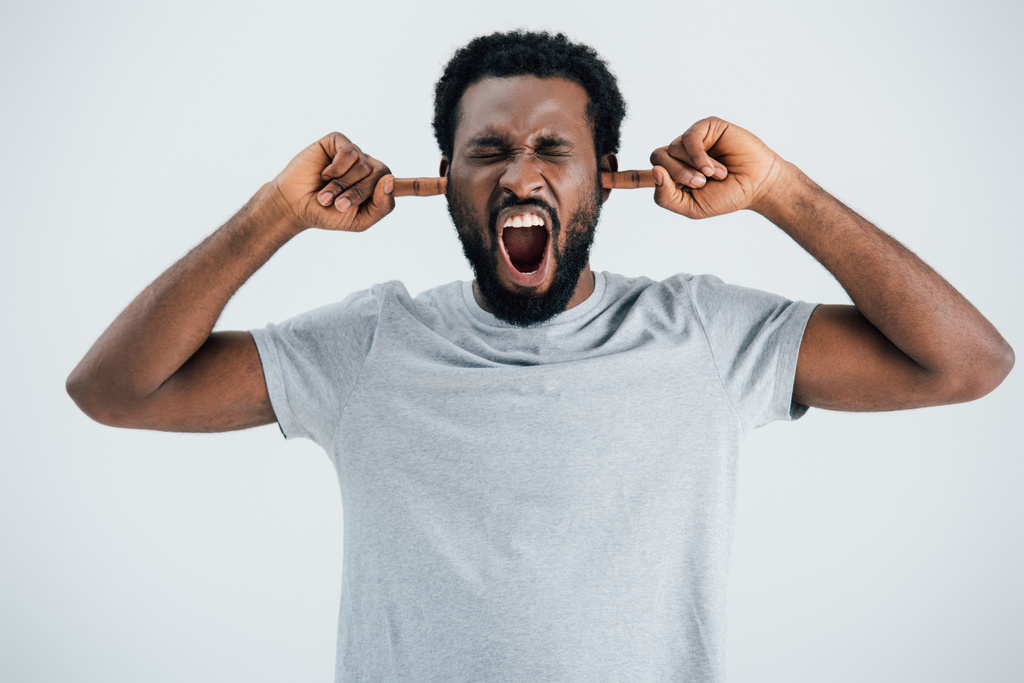 灰色のTシャツを着た感情的なアフリカ系アメリカ人男性が叫び、耳を閉じる - 写真・画像