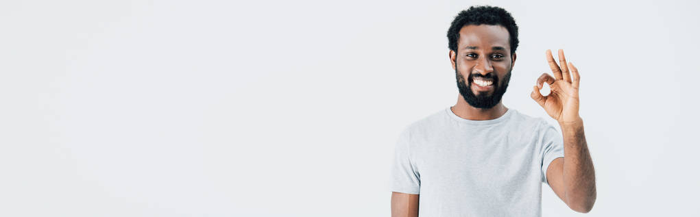 vrolijke African American man in grijs t-shirt toont OK teken geïsoleerd op grijs - Foto, afbeelding