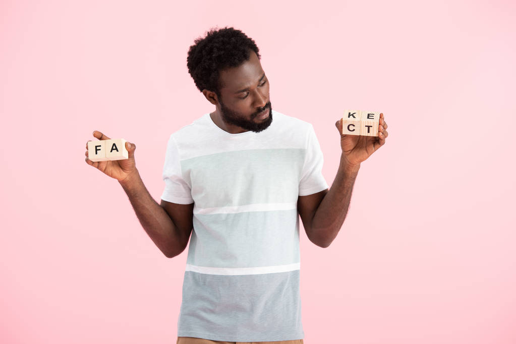 african american man looking at alphabet cubes with fact word, isolated on pink - Photo, Image