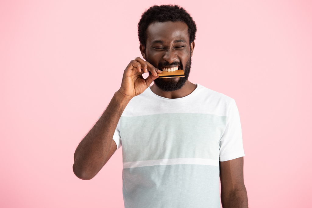 african american man biting credit card isolated on pink - Photo, Image