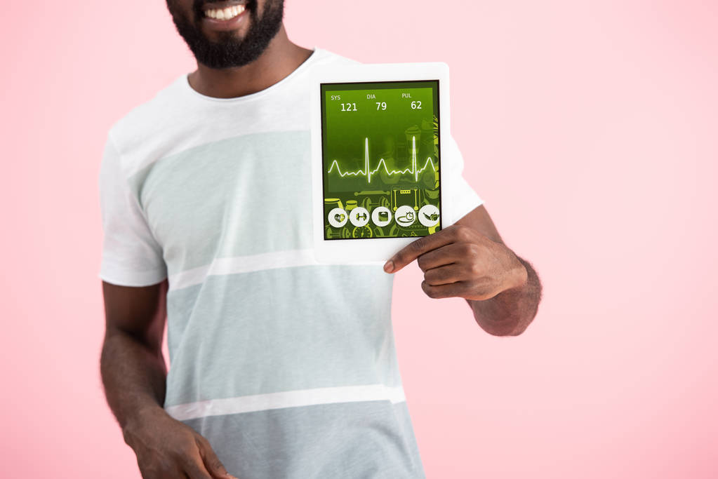 cropped view of smiling african american man showing digital tablet with health app, isolated on pink - Photo, Image