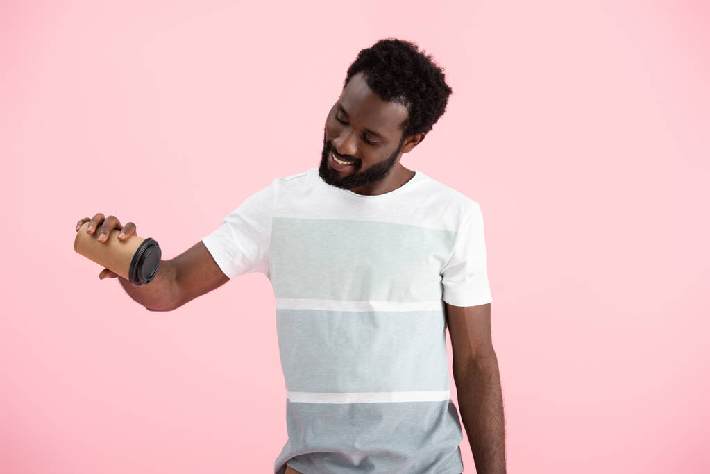 glimlachend Afro-Amerikaanse man houdt van koffie te gaan, geïsoleerd op roze - Foto, afbeelding
