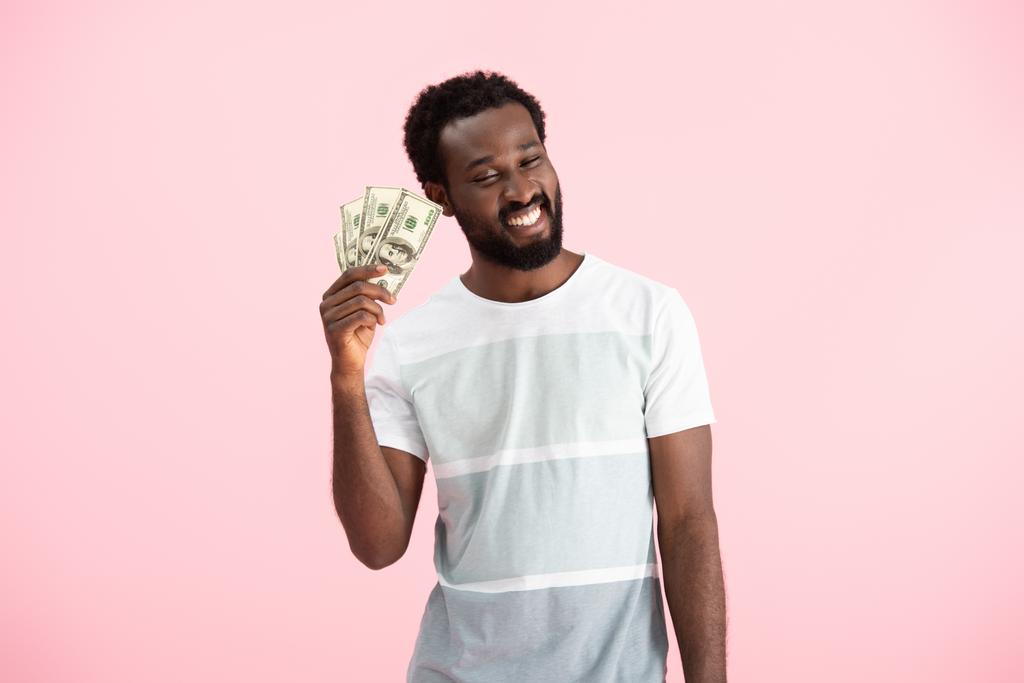 金の紙幣を持つ笑顔のアフリカ系アメリカ人男性、ピンクで孤立 - 写真・画像