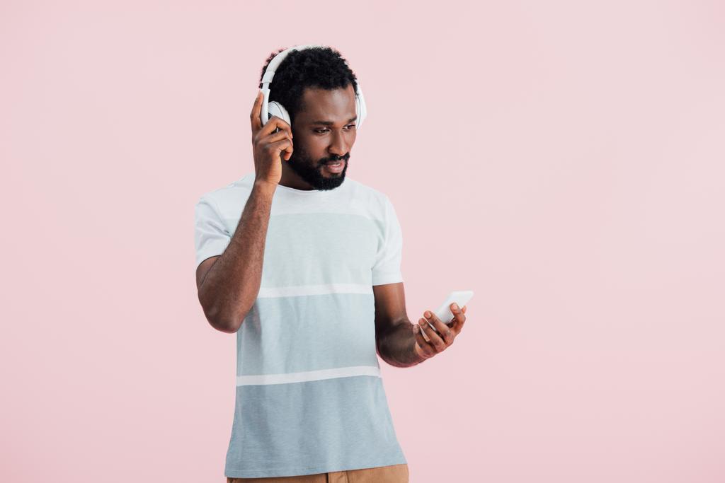 ヘッドフォンとスマートフォンで音楽を聴くアフリカ系アメリカ人男性、ピンクで隔離  - 写真・画像
