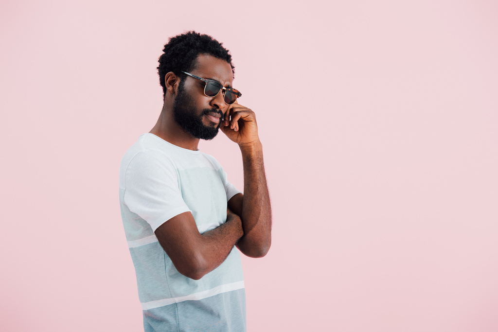 молодий задумливий афроамериканський чоловік в сонцезахисних окулярах, ізольований на рожевому
 - Фото, зображення