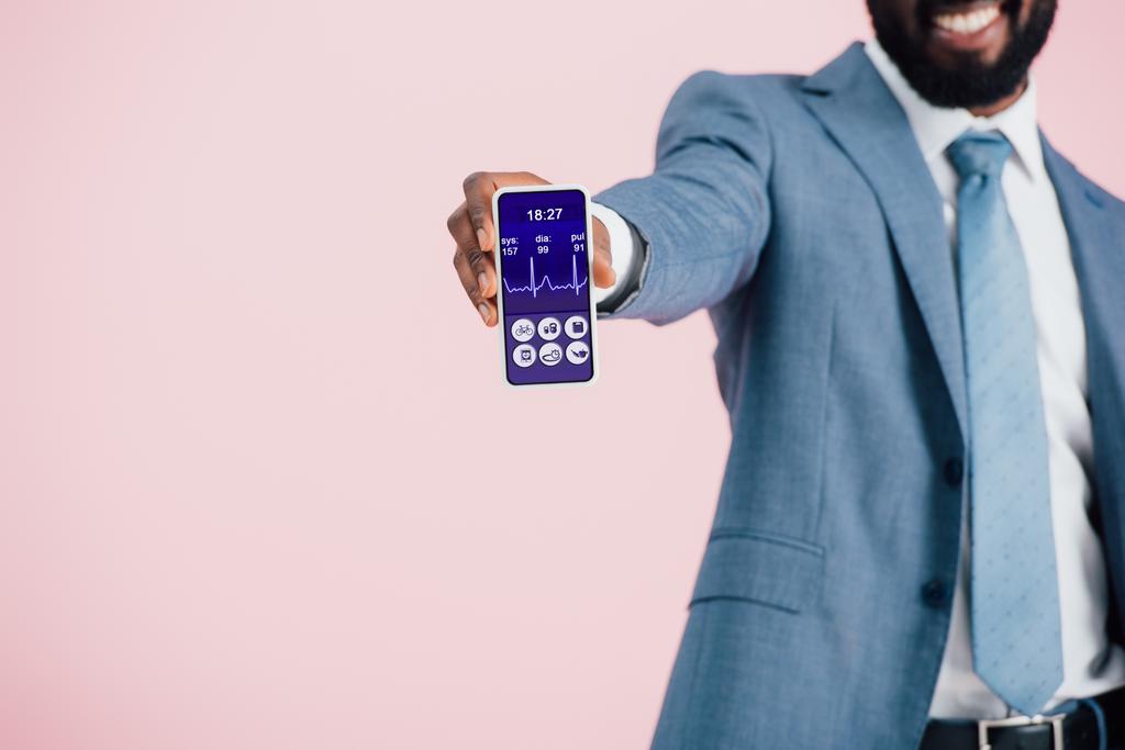 vista ritagliata di uomo d'affari afroamericano in giacca e cravatta mostrando smartphone con app salute, isolato su rosa
  - Foto, immagini