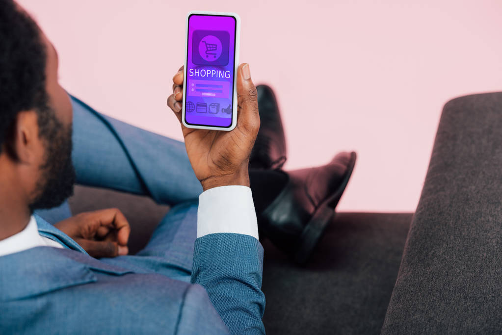 ショッピングアプリでスマートフォンを示すアフリカ系アメリカ人ビジネスマンのトリミングビュー,ピンクで隔離 - 写真・画像