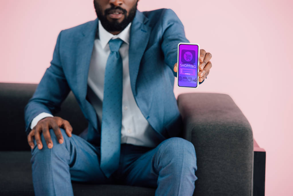 oříznutý pohled afrického amerického podnikatele zobrazující smartphone s nákupní aplikací, izolovaný na růžovém - Fotografie, Obrázek