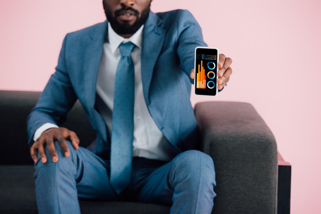 vista recortada del hombre de negocios afroamericano que muestra el teléfono inteligente con aplicación de infografía, aislado en rosa
 - Foto, imagen