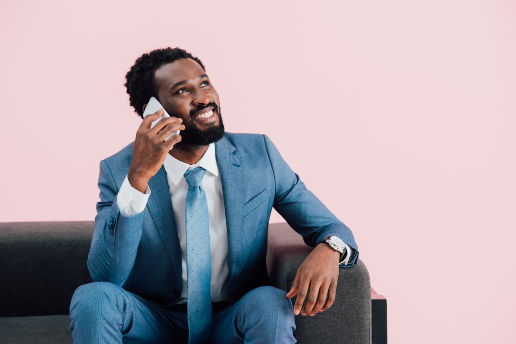 yakışıklı afro-amerikan işadamı koltukta oturan ve akıllı telefon konuşurken, pembe izole - Fotoğraf, Görsel