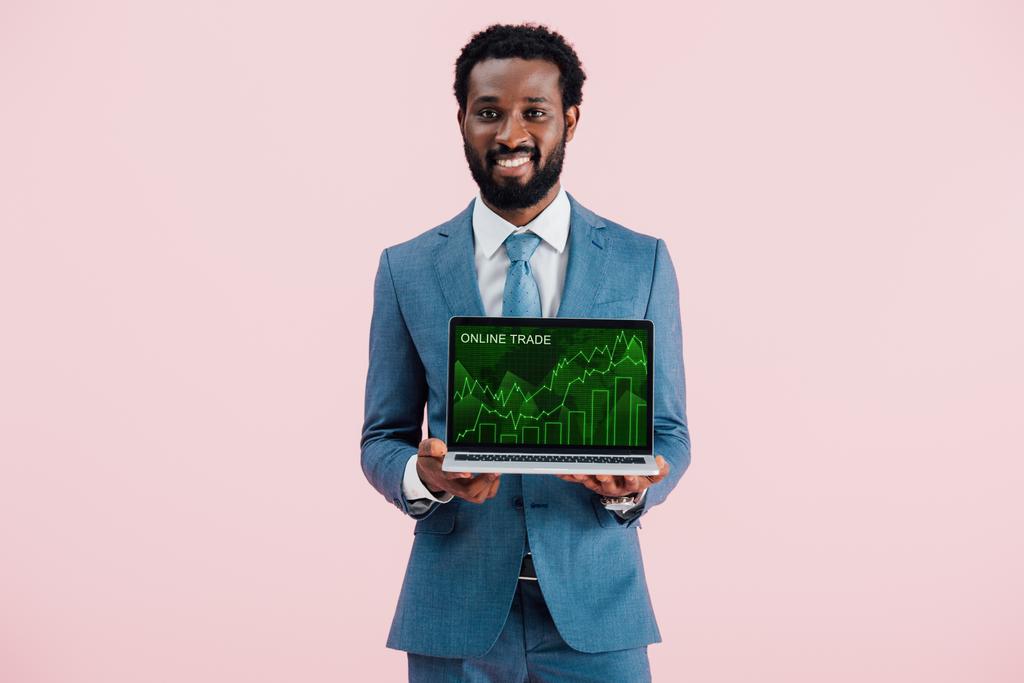 uśmiechnięty African American biznesmen pokazując laptopa z handlem online na niebiesko - Zdjęcie, obraz