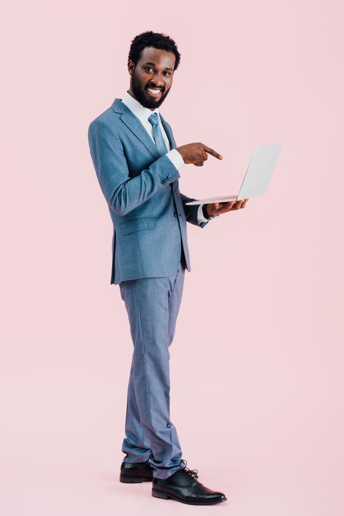 hymyilevä afrikkalainen amerikkalainen liikemies osoittaa kannettavan eristetty vaaleanpunainen
 - Valokuva, kuva
