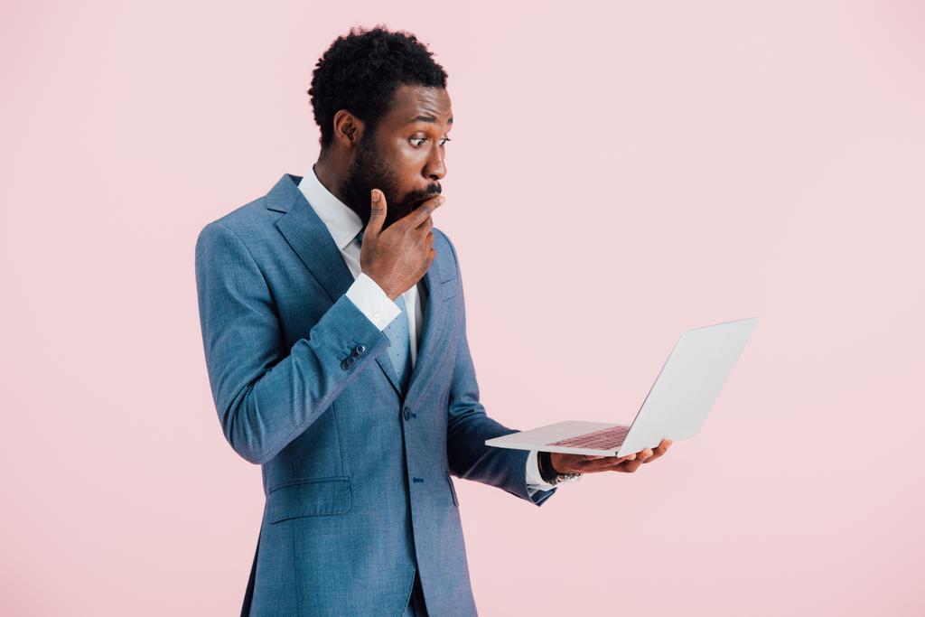 wstrząśnięty African American biznesmen za pomocą laptopa izolowane na różowy - Zdjęcie, obraz