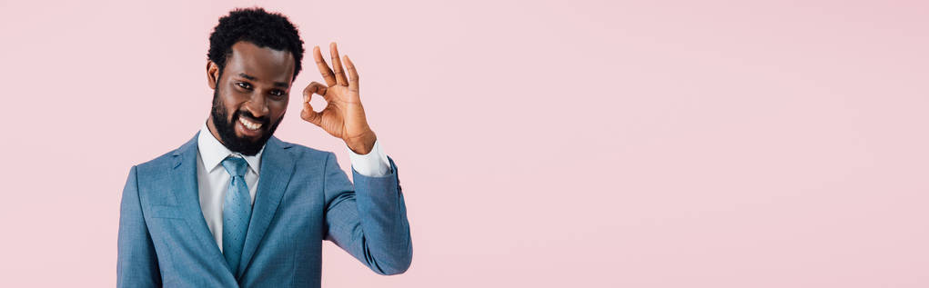 веселий афроамериканець бізнесмен в костюмі показані OK знак, ізольований на рожевому - Фото, зображення