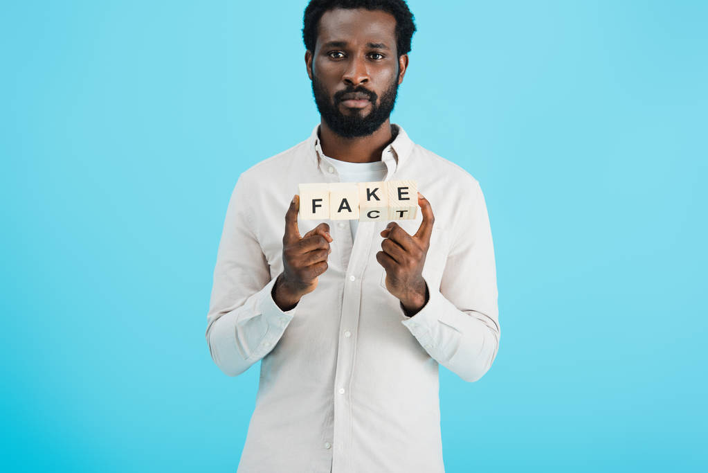 серьезный африканский американец держит кубики алфавита с фактом слово, изолированные на синий
 - Фото, изображение