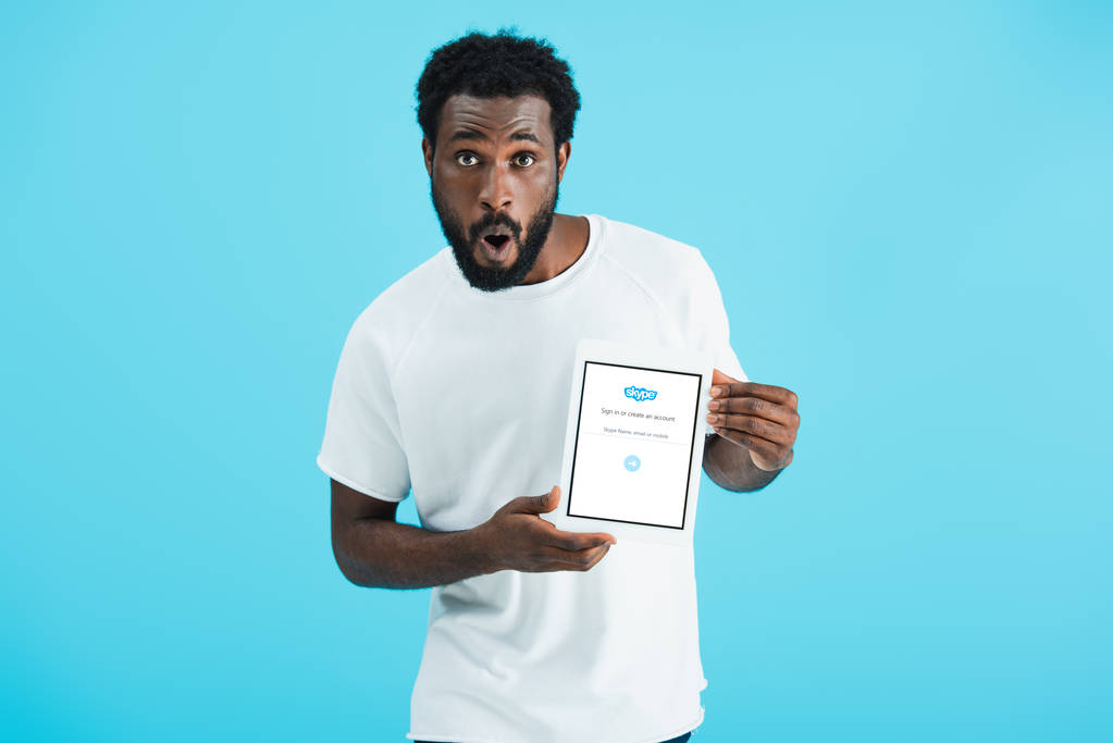 Kyiv, Ukrajna-május 17, 2019: meglepett afro-amerikai férfi bemutató digitális tabletta a Skype app, elszigetelt kék - Fotó, kép