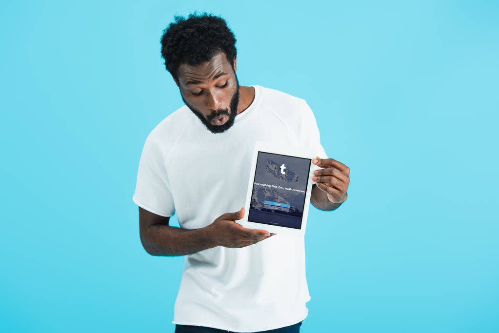 KYIV, UCRANIA - 17 de mayo de 2019: sorprendido hombre afroamericano mirando la tableta digital con aplicación tumblr, aislado en azul
 - Foto, Imagen