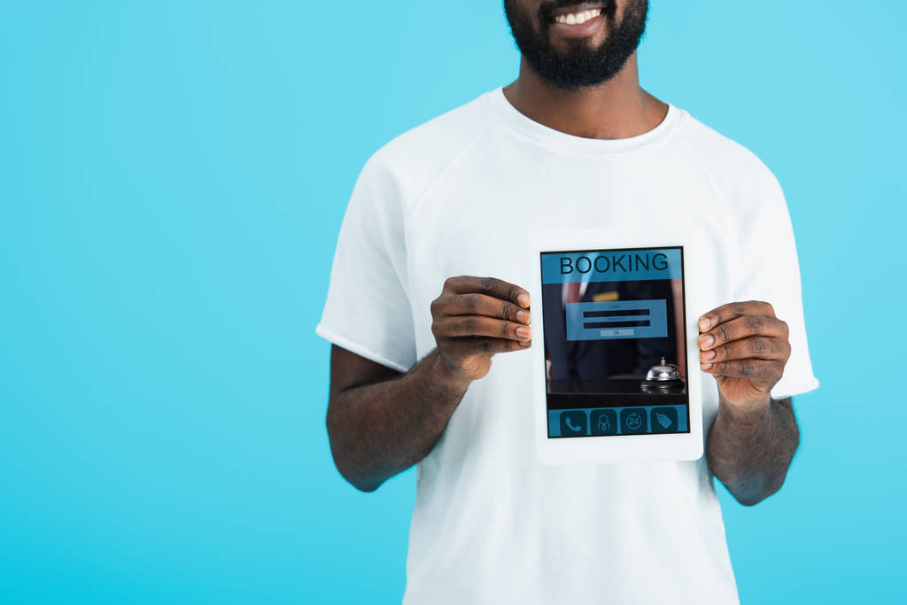 予約アプリでデジタルタブレットを示すアフリカ系アメリカ人男性のトリミングビュー, 青で隔離 - 写真・画像